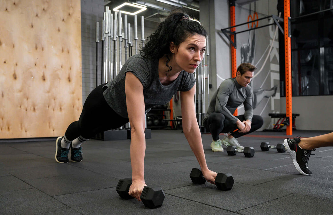 Person doing plank exercise with dumbbells in gym, focusing on optimal tempo and strength using gym equipment.