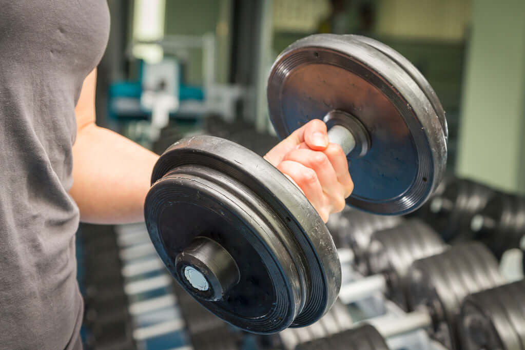 Person gripping a dumbbell in gym to improve strength with gym equipment.