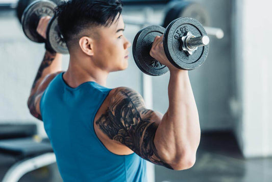 Man performing shoulder press with dumbbells in gym, showcasing effective upper body workout using gym equipment.