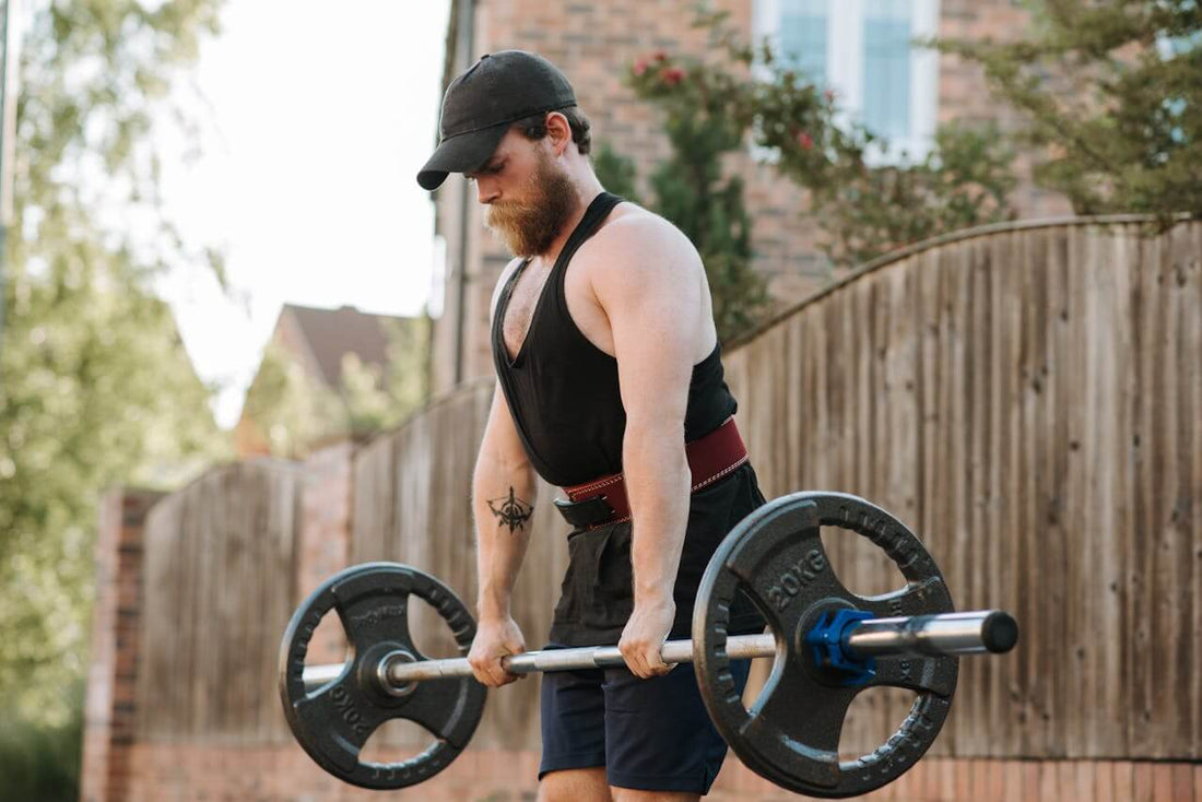 Man lifting barbell wearing weight belt in outdoor gym setting