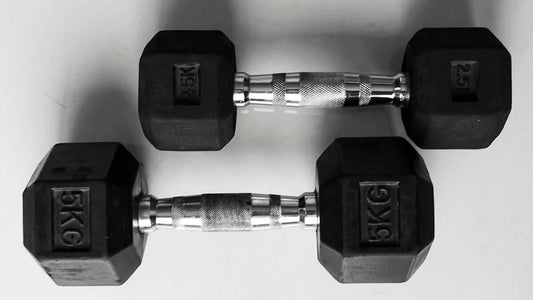 Black hexagonal dumbbells weighing 5 kg each on a white surface, ideal for building muscle and enhancing gym equipment variety.