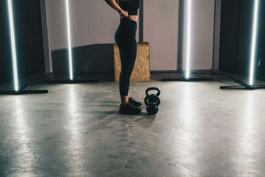 Woman ready to lift kettlebell in gym, showcasing strength training with kettlebells, resistance bands, and other gym equipment.