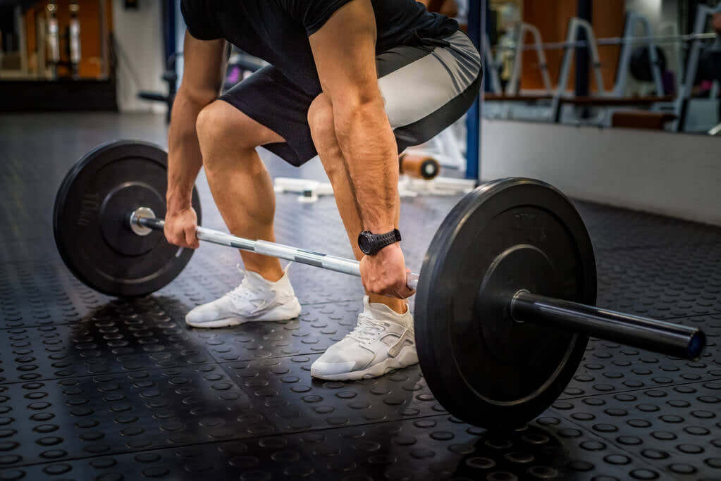 Person performing deadlift with a barbell in a gym, highlighting lower body strength exercises for core and legs.