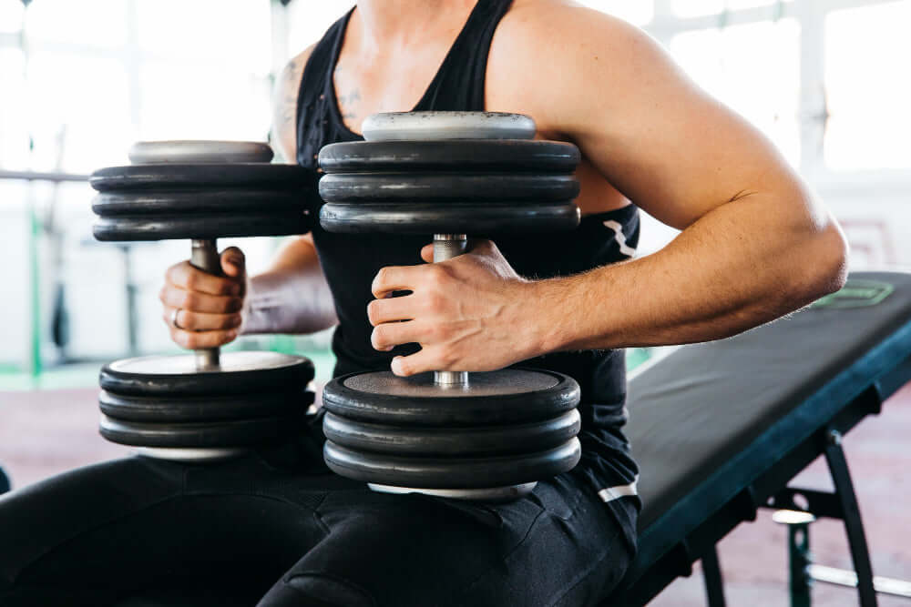 Man holding modern adjustable dumbbells in a gym setting for versatile home fitness workout.